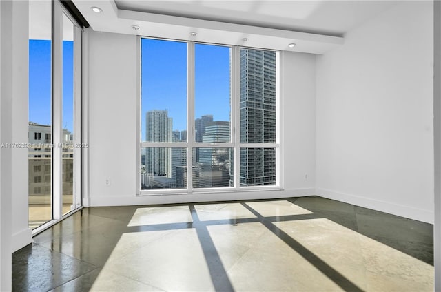 spare room with floor to ceiling windows, a city view, recessed lighting, and baseboards