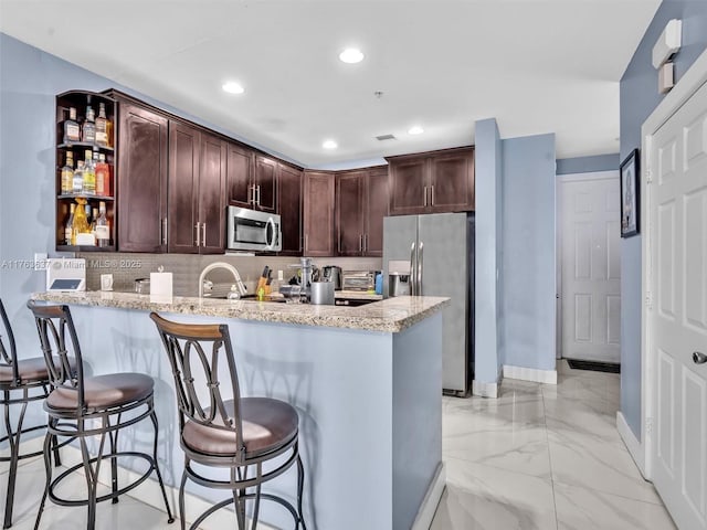 kitchen featuring a peninsula, decorative backsplash, dark brown cabinets, appliances with stainless steel finishes, and marble finish floor