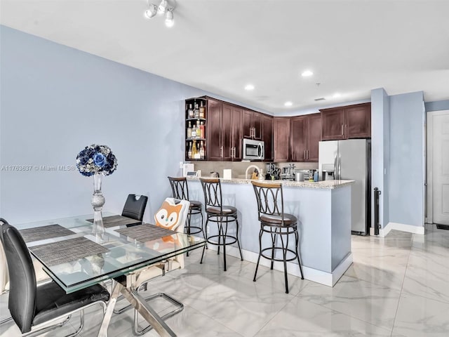 kitchen with marble finish floor, a breakfast bar, appliances with stainless steel finishes, a peninsula, and light stone countertops