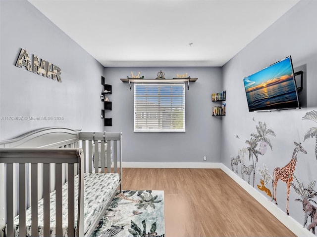 bedroom with baseboards, a nursery area, and wood finished floors