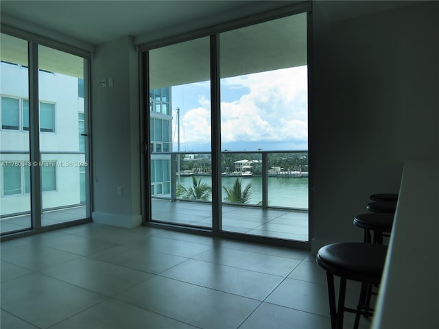 tiled empty room featuring a wall of windows, baseboards, and a water view