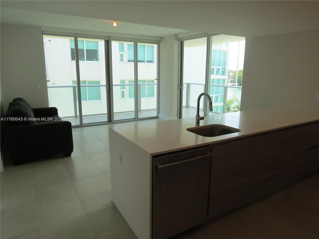 kitchen with light tile patterned floors, dishwashing machine, light countertops, and a sink