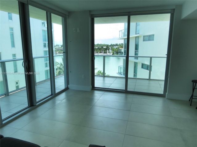 empty room with tile patterned floors, floor to ceiling windows, baseboards, and a water view