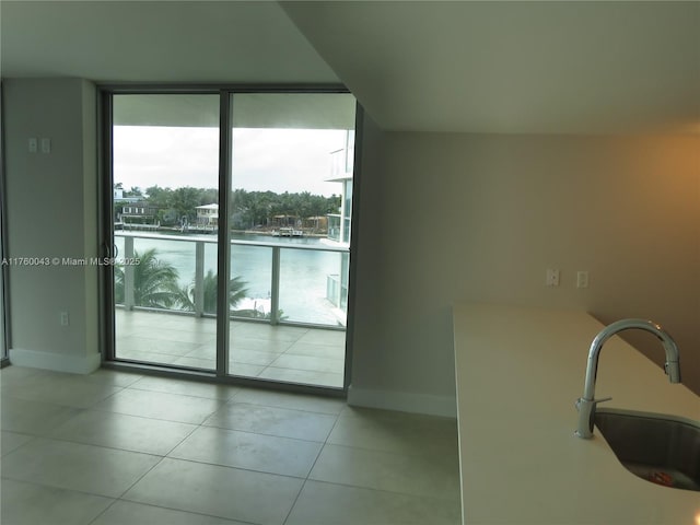 interior space with a water view, a sink, tile patterned flooring, a wall of windows, and baseboards