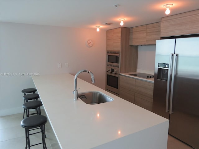 kitchen featuring a breakfast bar, light countertops, appliances with stainless steel finishes, and a sink