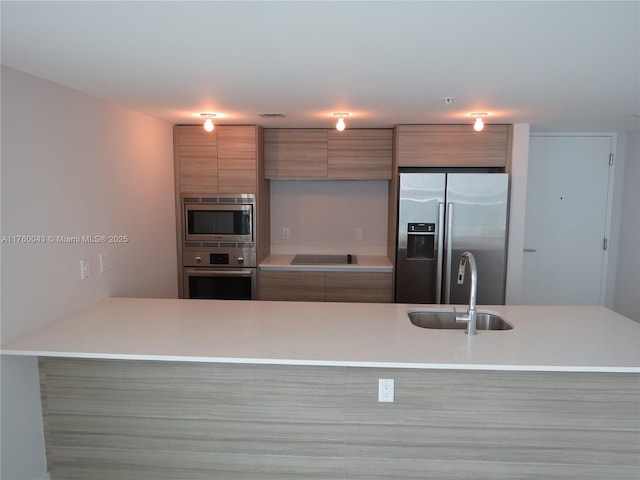 kitchen with a sink, light countertops, brown cabinets, stainless steel appliances, and modern cabinets