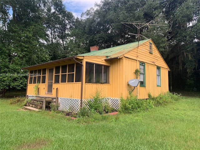 view of property exterior with a lawn, a chimney, and a sunroom