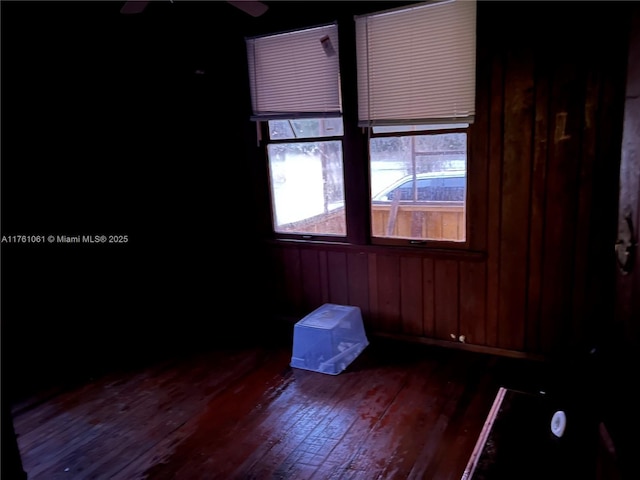 unfurnished room with wooden walls, a ceiling fan, and dark wood-style flooring