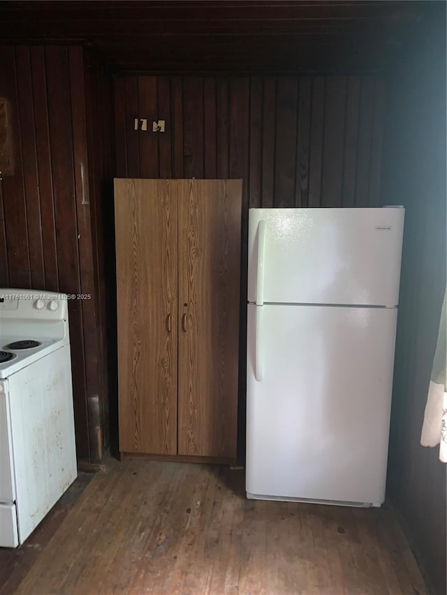 kitchen featuring wood walls, white appliances, and wood finished floors