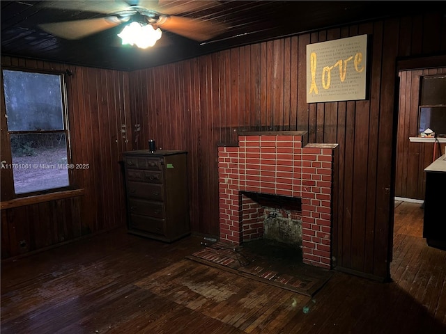 living room with hardwood / wood-style floors, a tiled fireplace, a ceiling fan, and wood walls