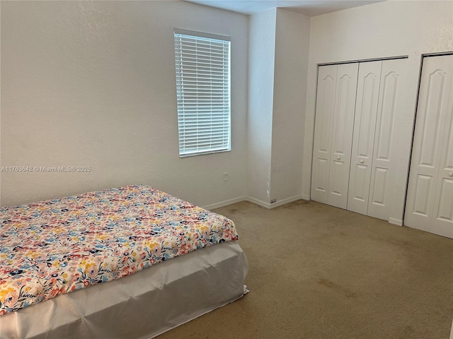 bedroom with light colored carpet, baseboards, and two closets