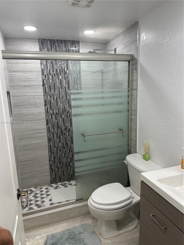 bathroom featuring visible vents, toilet, a shower stall, vanity, and a textured wall