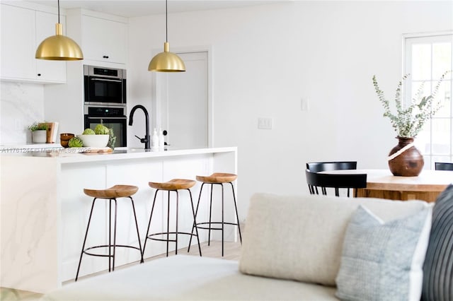 kitchen with a sink, hanging light fixtures, white cabinetry, double oven, and a kitchen breakfast bar