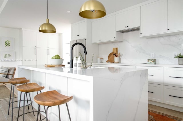 kitchen featuring white cabinetry, a kitchen breakfast bar, backsplash, and under cabinet range hood