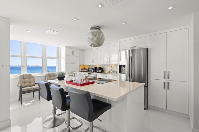 kitchen with black electric stovetop, stainless steel fridge with ice dispenser, white cabinetry, a kitchen breakfast bar, and a center island