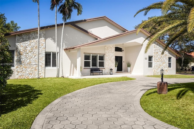 back of house featuring stone siding, stucco siding, curved driveway, and a yard