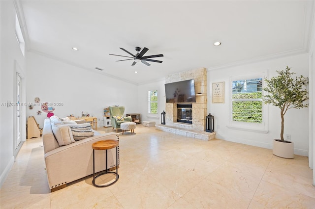 living room with a stone fireplace, crown molding, a ceiling fan, and a healthy amount of sunlight