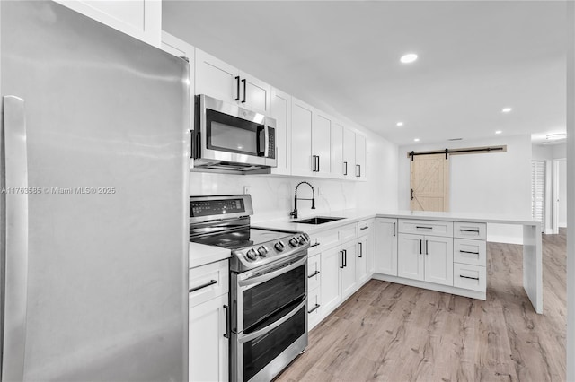 kitchen with a sink, a barn door, appliances with stainless steel finishes, a peninsula, and light wood finished floors