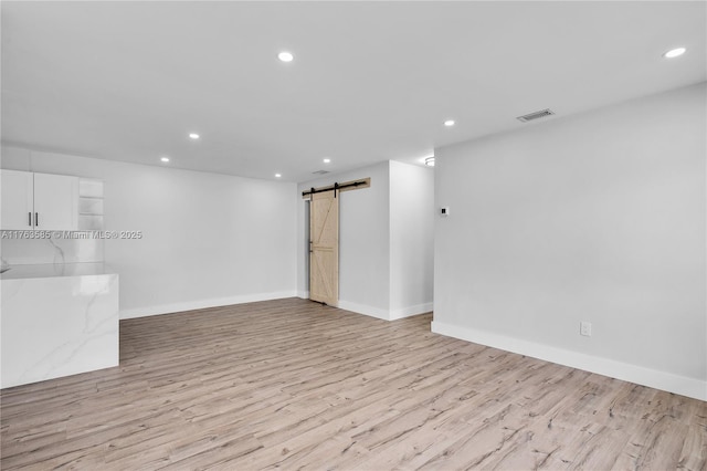 empty room featuring visible vents, recessed lighting, a barn door, light wood-style floors, and baseboards