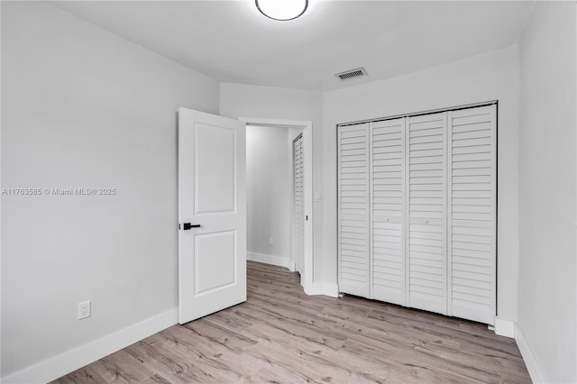 unfurnished bedroom with a closet, visible vents, baseboards, and wood finished floors