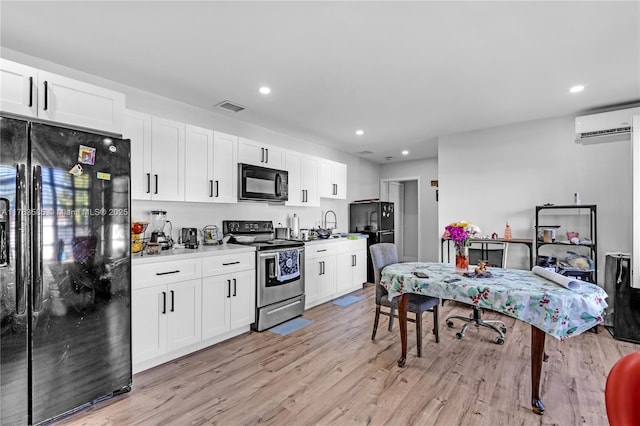 kitchen with light wood-type flooring, visible vents, black appliances, a wall mounted AC, and white cabinetry