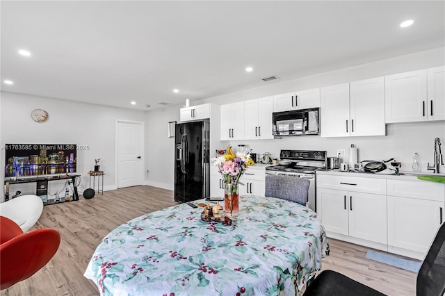 kitchen with light countertops, recessed lighting, light wood-style flooring, white cabinets, and black appliances