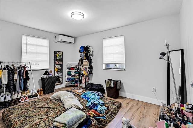 bedroom featuring multiple windows, wood finished floors, baseboards, and a wall mounted AC