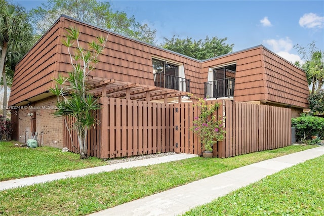 view of side of home featuring brick siding, a fenced front yard, a lawn, mansard roof, and a gate