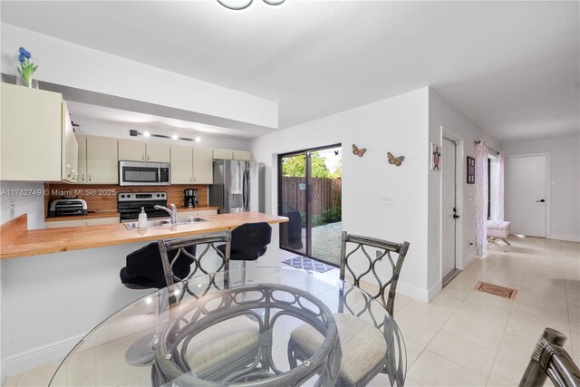 kitchen featuring cream cabinetry, a sink, appliances with stainless steel finishes, a peninsula, and light tile patterned flooring