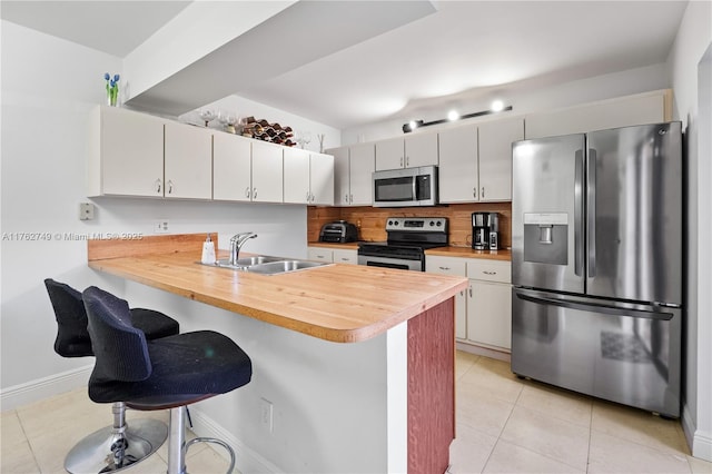 kitchen featuring backsplash, a peninsula, light tile patterned flooring, stainless steel appliances, and a sink