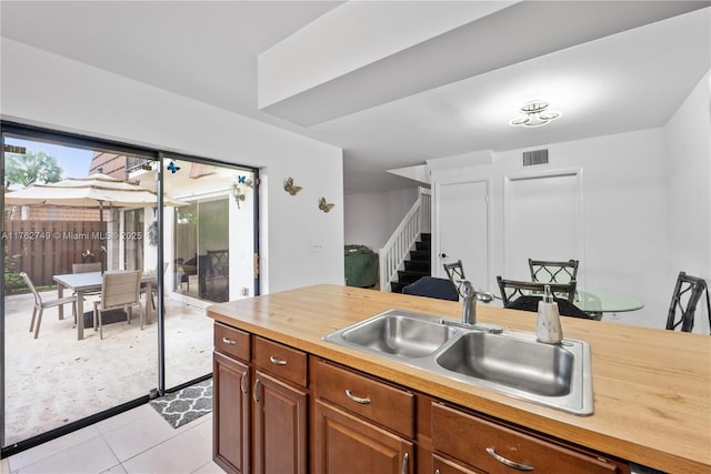 kitchen with visible vents, butcher block countertops, brown cabinets, light tile patterned flooring, and a sink