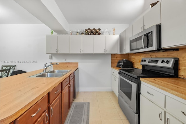 kitchen with backsplash, light tile patterned floors, stainless steel appliances, wood counters, and a sink