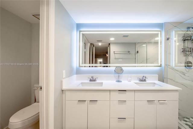 full bath featuring double vanity, a marble finish shower, toilet, and a sink