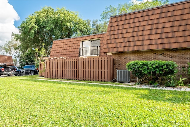 exterior space featuring a yard, cooling unit, brick siding, and mansard roof