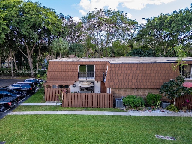 view of front facade featuring a front yard, central AC unit, fence, mansard roof, and brick siding