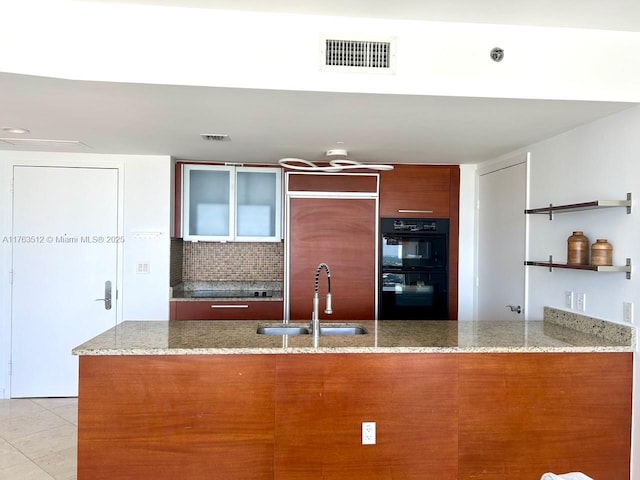 kitchen with visible vents, a peninsula, a sink, dobule oven black, and brown cabinets