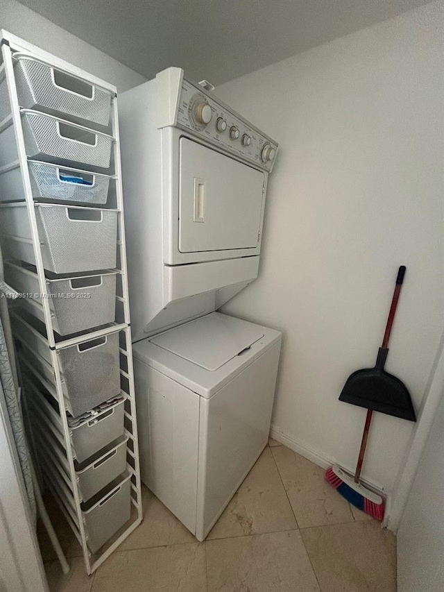 clothes washing area featuring light tile patterned floors, laundry area, stacked washer / dryer, and baseboards