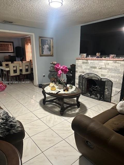 living area with a tiled fireplace, visible vents, and a textured ceiling