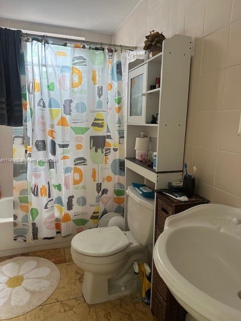 full bath with toilet, tile walls, a shower with shower curtain, and a sink