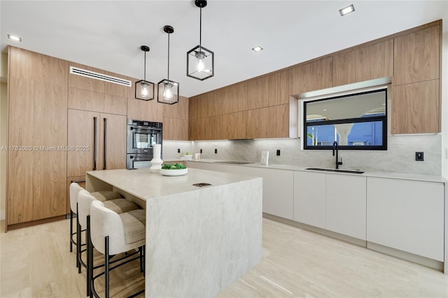 kitchen featuring a sink, a kitchen breakfast bar, double wall oven, and modern cabinets