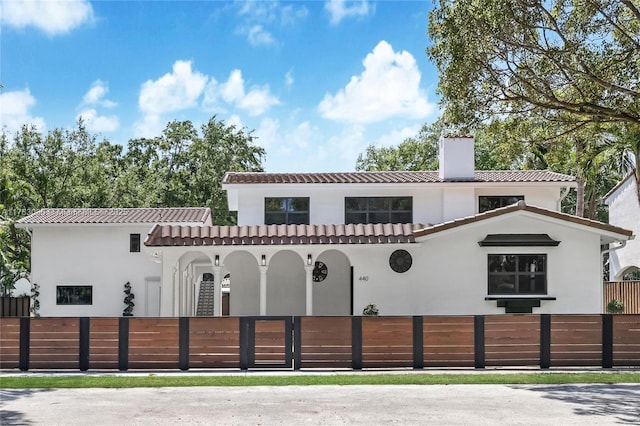 mediterranean / spanish house featuring a tile roof, a chimney, a fenced front yard, and stucco siding