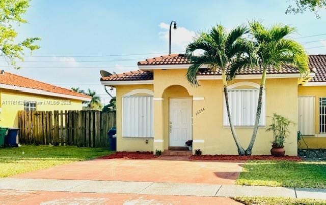 view of front facade with a front lawn, a tiled roof, fence, and stucco siding