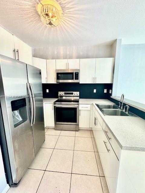 kitchen featuring light tile patterned flooring, white cabinets, appliances with stainless steel finishes, and a sink