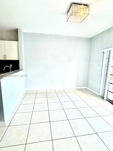 empty room featuring light tile patterned floors, baseboards, and a sink