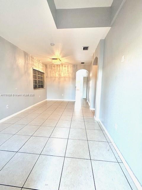 spare room featuring light tile patterned floors, visible vents, arched walkways, and baseboards