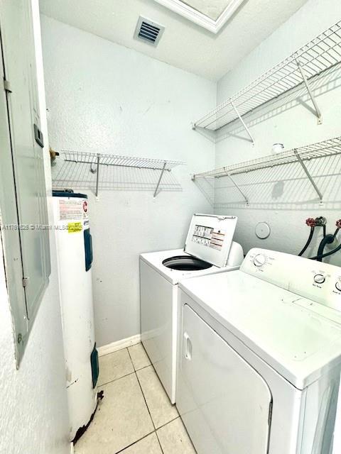 laundry area with light tile patterned floors, visible vents, laundry area, water heater, and washing machine and dryer