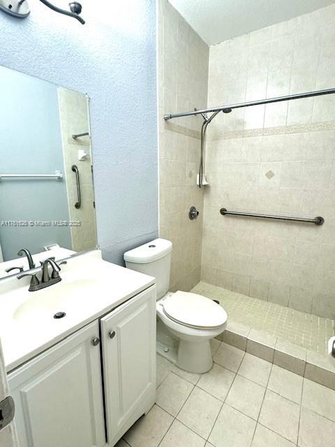 bathroom featuring tile patterned floors, toilet, tiled shower, and vanity