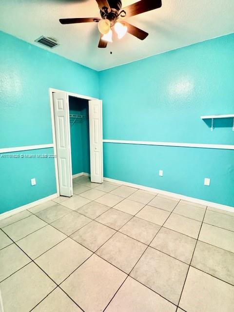 unfurnished bedroom with light tile patterned floors, a ceiling fan, visible vents, baseboards, and a closet