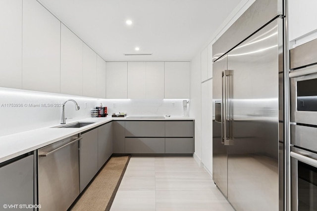 kitchen with modern cabinets, gray cabinets, a sink, appliances with stainless steel finishes, and light countertops