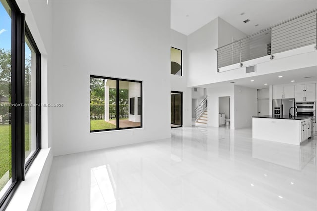 unfurnished living room with stairway, a high ceiling, visible vents, and a sink